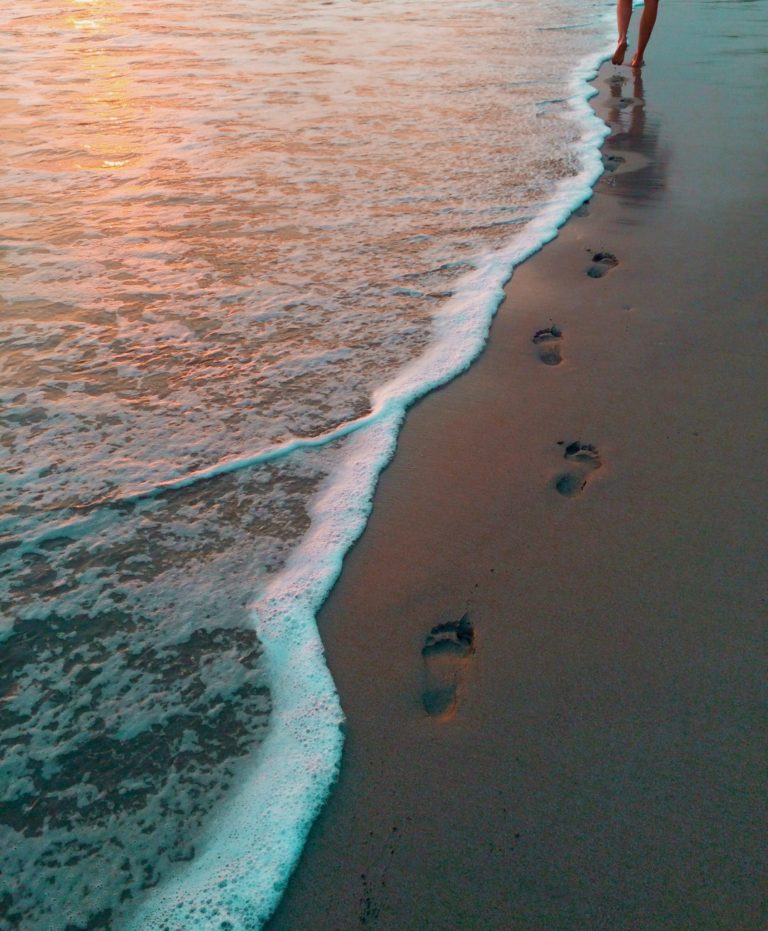 Footprints in the sand near a gentle wave with lighting from a setting sun